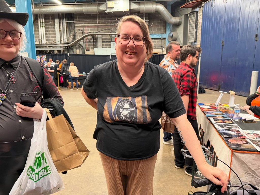 Photograph of Helen Rose Thwaite. She wears a black t-shirt, beige trousers, and a very silly grin
