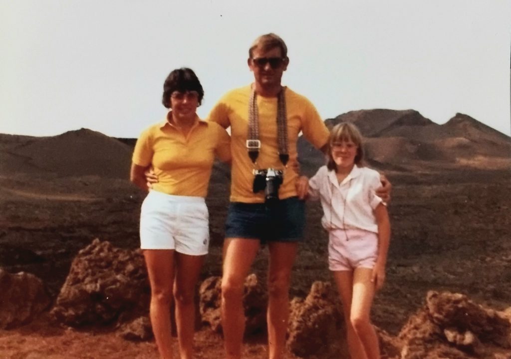 Photograph of a dark-haired woman and man, with a blond-haired child of around 11 years old, against the backdrop of the countryside